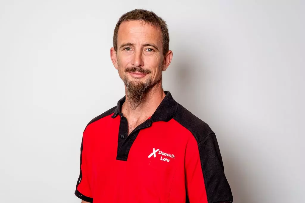 Gerüstbauer Dominic Lohr steht vor einer weißen Wand und schaut lächelnd in die Kamera.