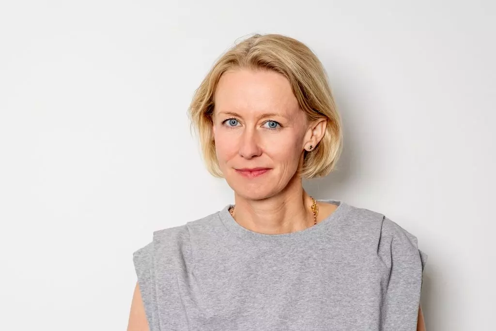Stefanie Eikel steht vor einer weißen Wand und schaut lächelnd in die Kamera.